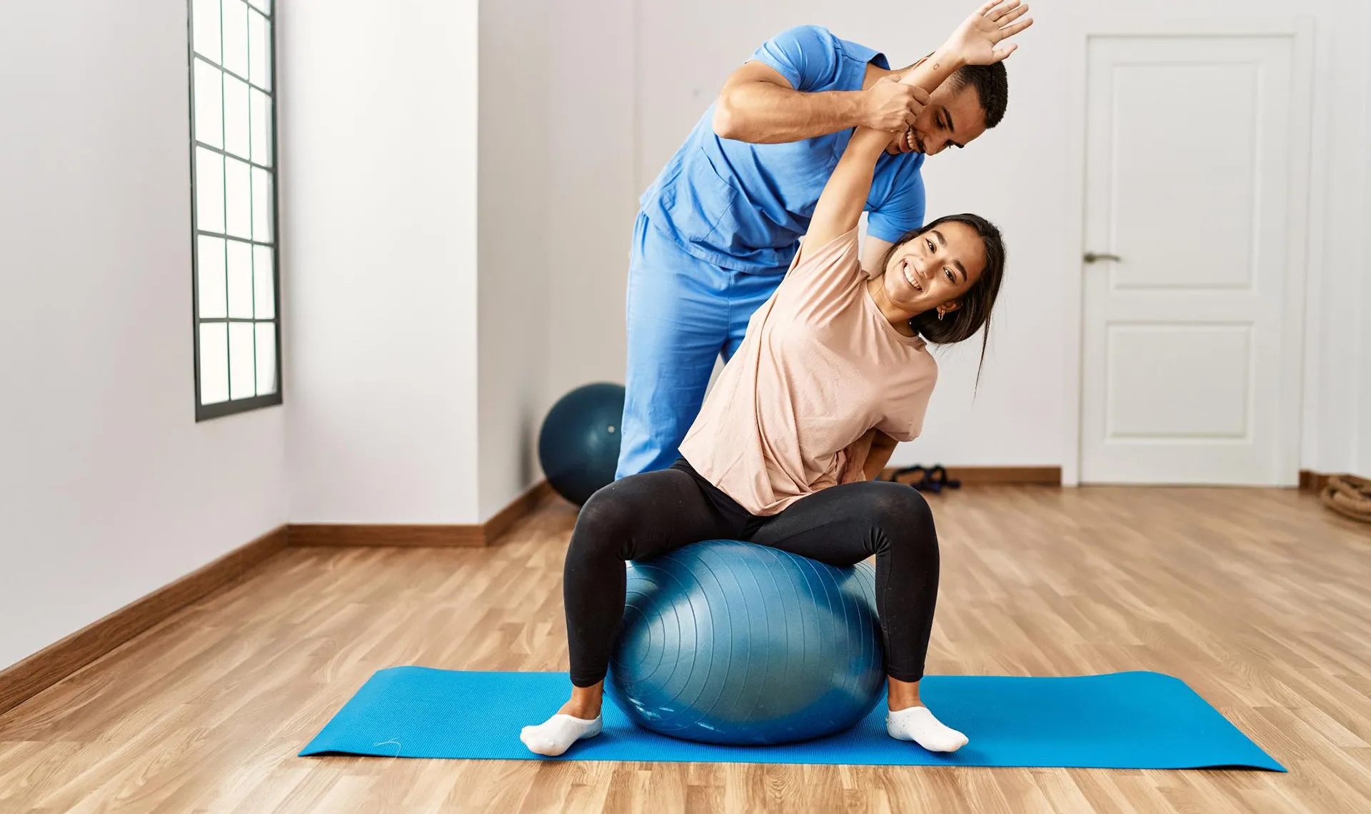 Bewegungstherapie im Reha-Zentrum Saalfelden – Physiotherapeut unterstützt Patientin bei Dehnübung auf Gymnastikball